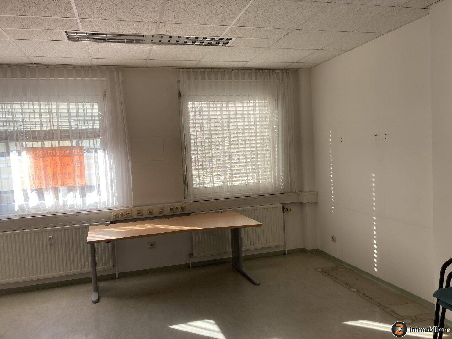 Helles Büro mit einem Schreibtisch und zwei Fenstern, die viel natürliches Licht hereinlassen.