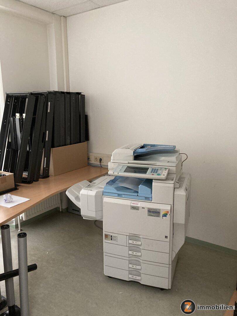 Büro mit einem großen Multifunktionsdrucker und einem Schreibtisch, bereit für den sofortigen Einsatz.