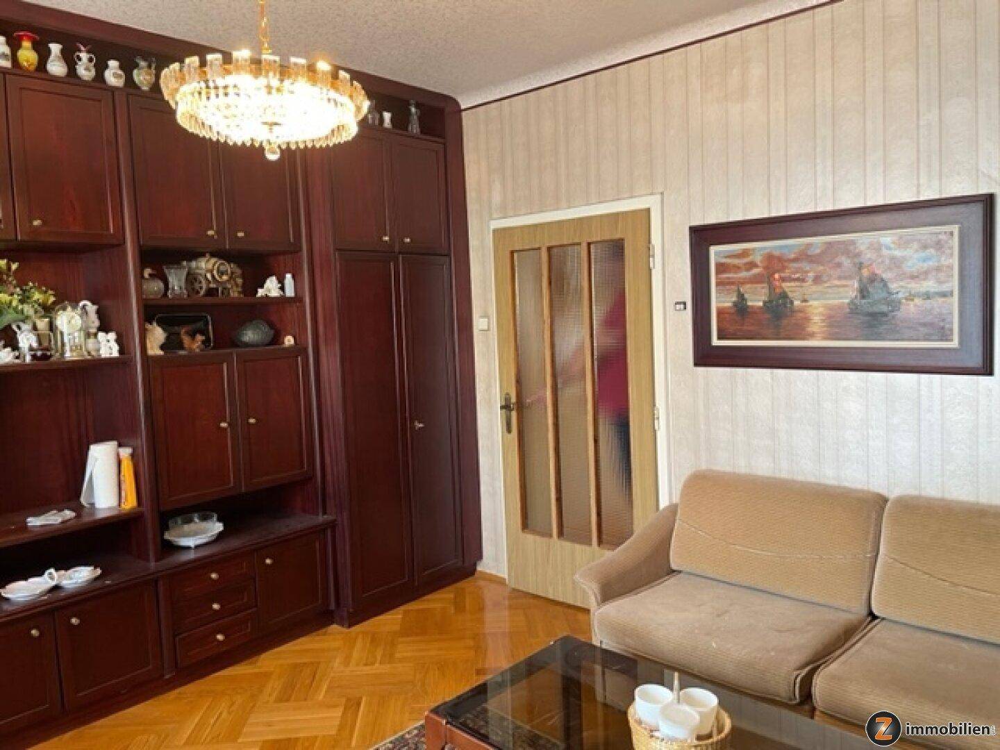 Wohnzimmer mit bequemer Couch, Couchtisch und großer Holzschrankwand auf Parkettboden.
