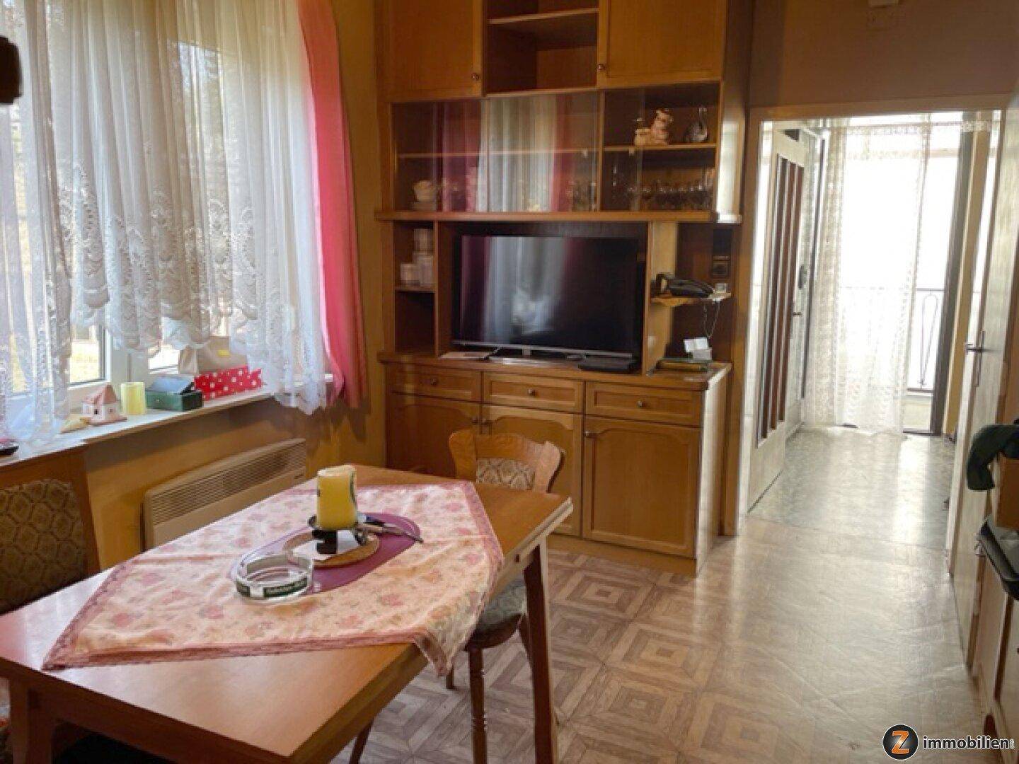 Traditioneller Wohn-Essbereich mit Holzschrank, Fernseher und Zugang zu einem Balkon.