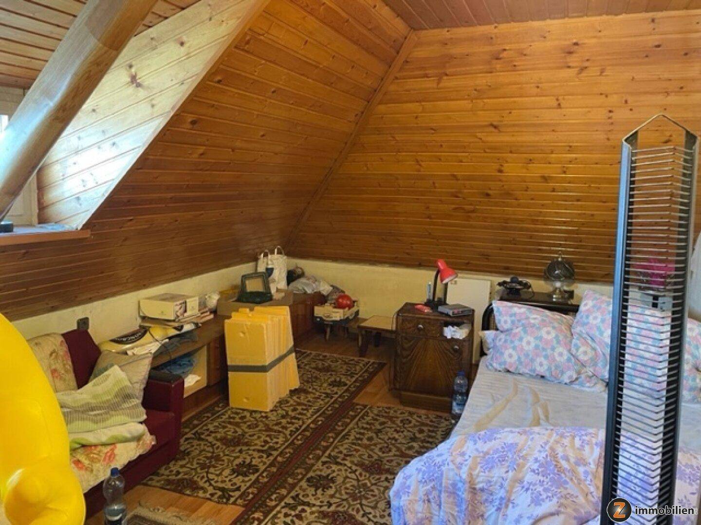 Dachgeschosszimmer mit schrägen Holzdecken und -wänden, genutzt als Schlaf- und Abstellraum.
