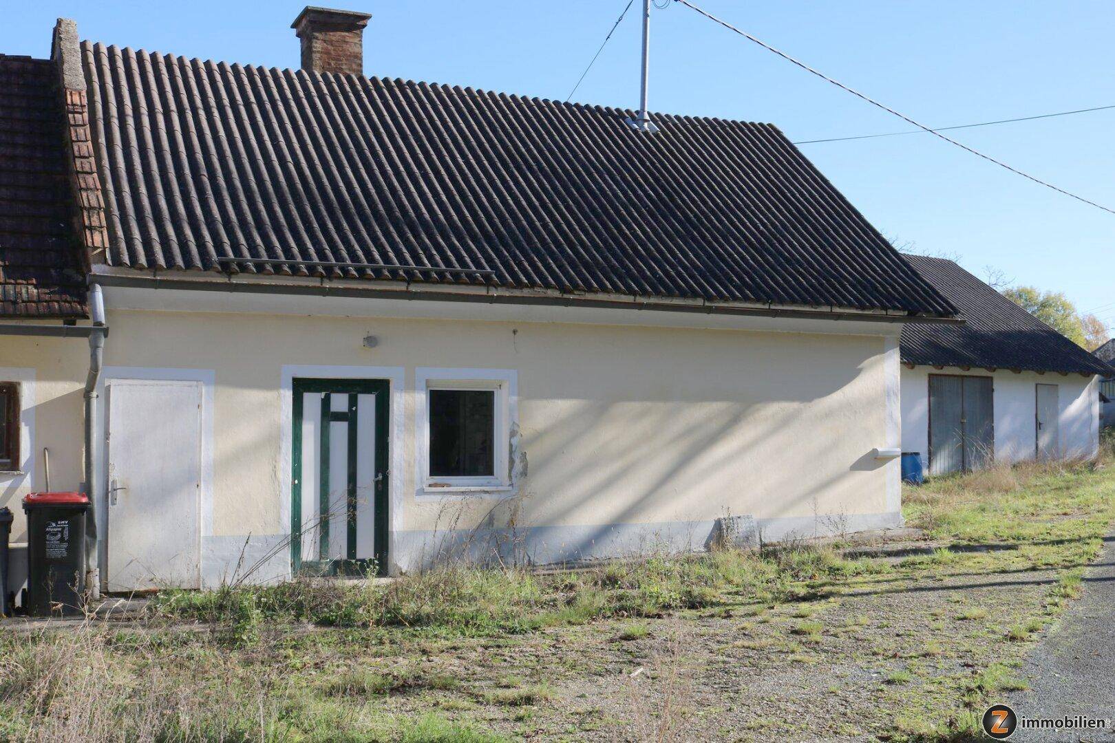 Seitenansicht eines ländlichen Hauses mit einfacher Fassade, grüner Tür und dunklem Wellblechdach.