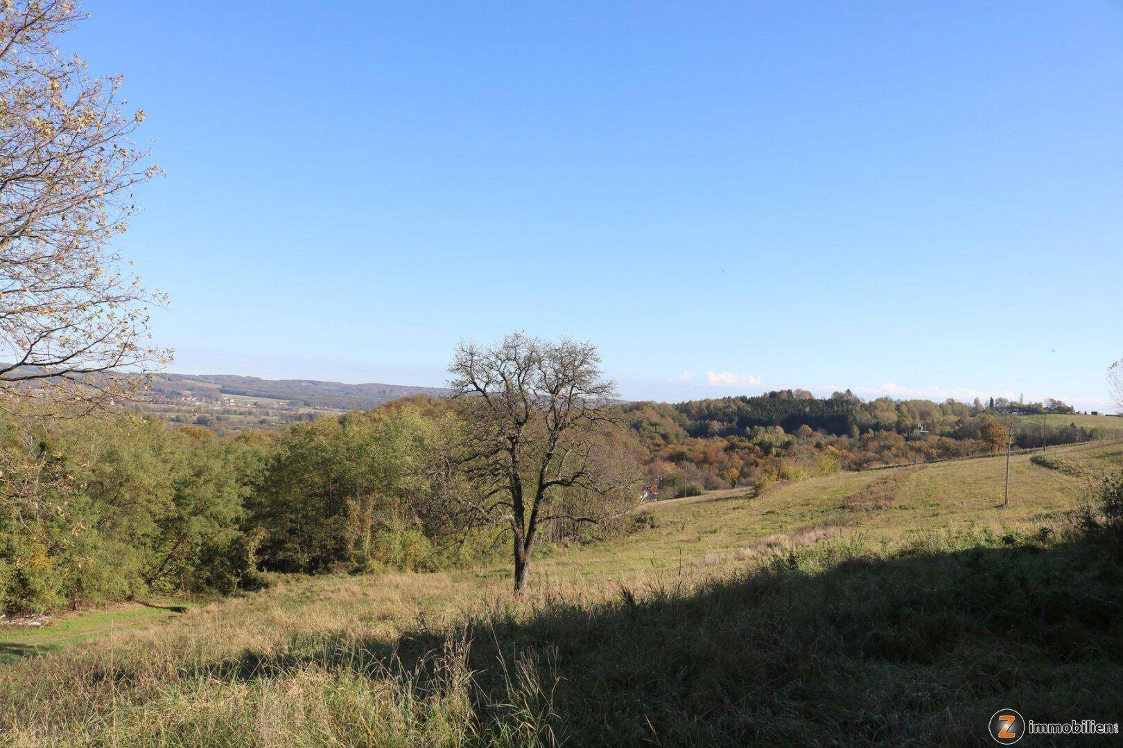Weitläufige hügelige Landschaft mit herbstlichen Bäumen und Feldern unter klarem blauem Himmel.