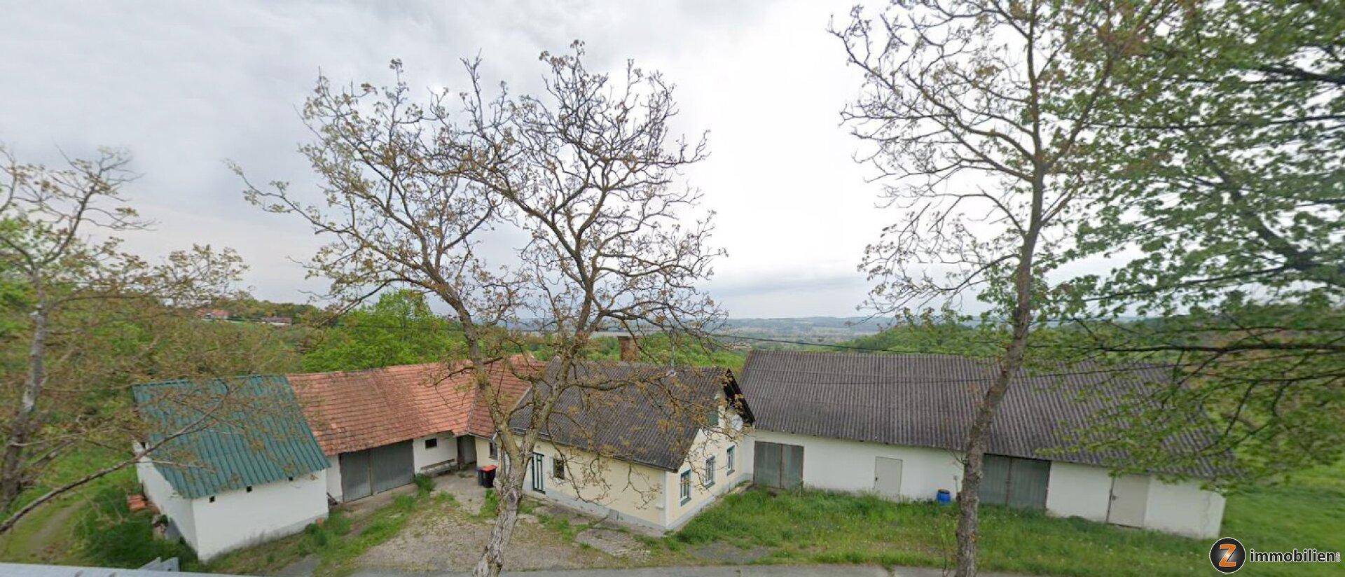 Luftaufnahme von mehreren ländlichen Gebäuden mit verschiedenen Dächern, umgeben von Bäumen und Feldern.