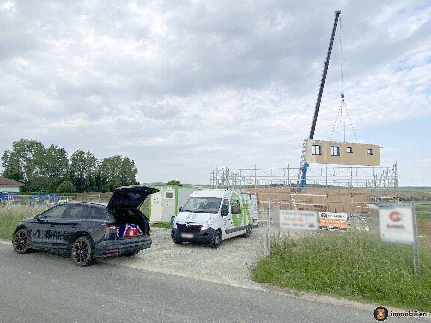 Baustelle eines neuen Holzhauses mit Kran und Gerüst in ländlicher Umgebung.