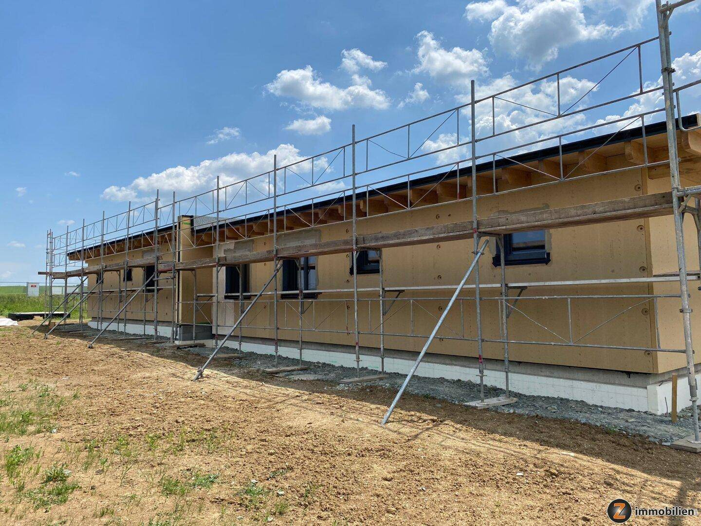 Baustelle eines modernen Holzhauses mit Gerüst und vorbereiteter Fassade.