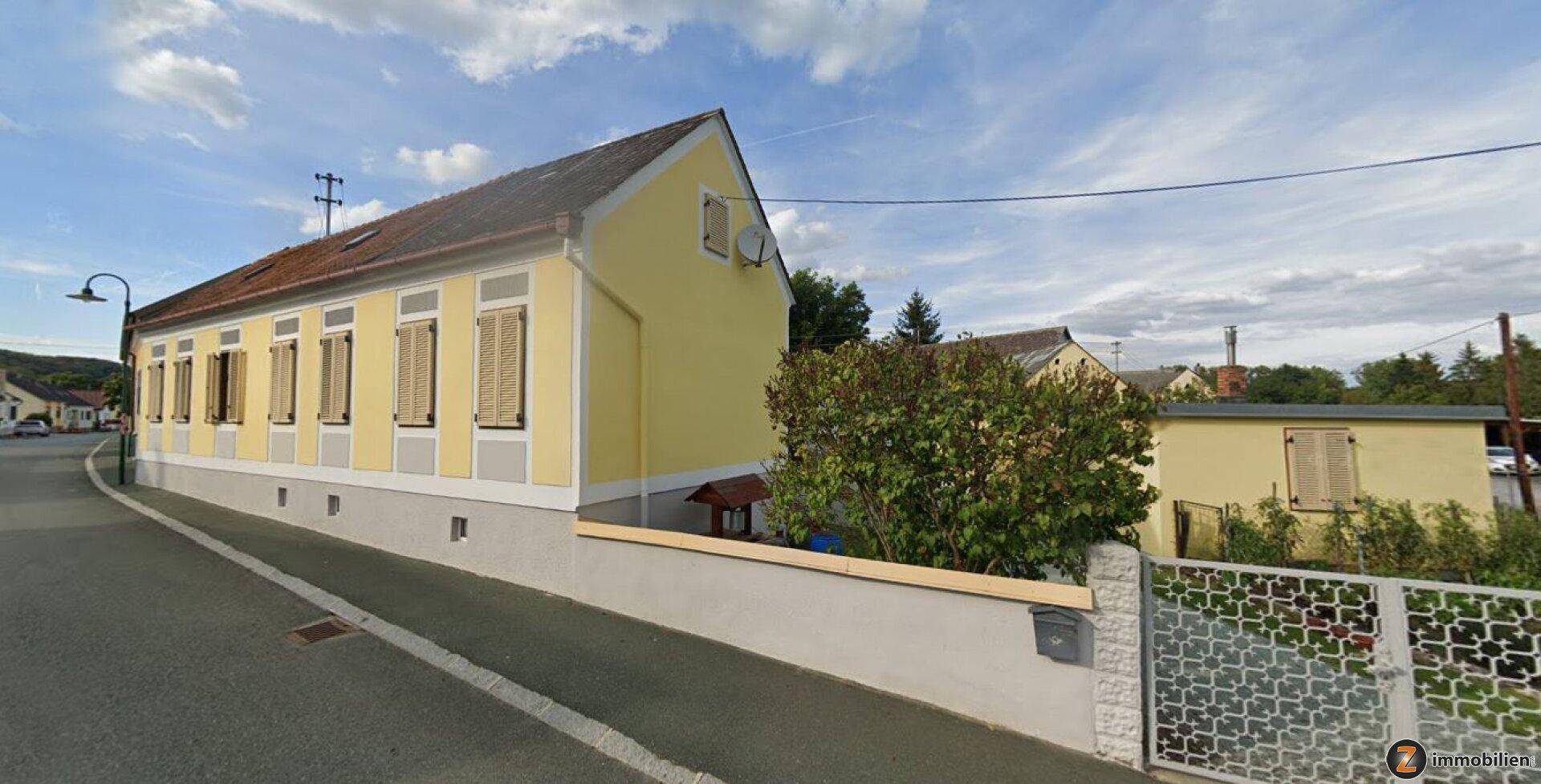 Gelbes Wohnhaus mit traditionellen Fensterläden und einem Vorgarten an einer ländlichen Straße.