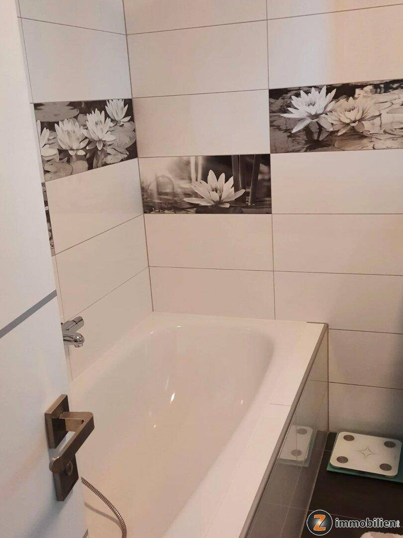 Helles Badezimmer mit Badewanne und dekorativen Fliesen mit Seerosenmotiv.