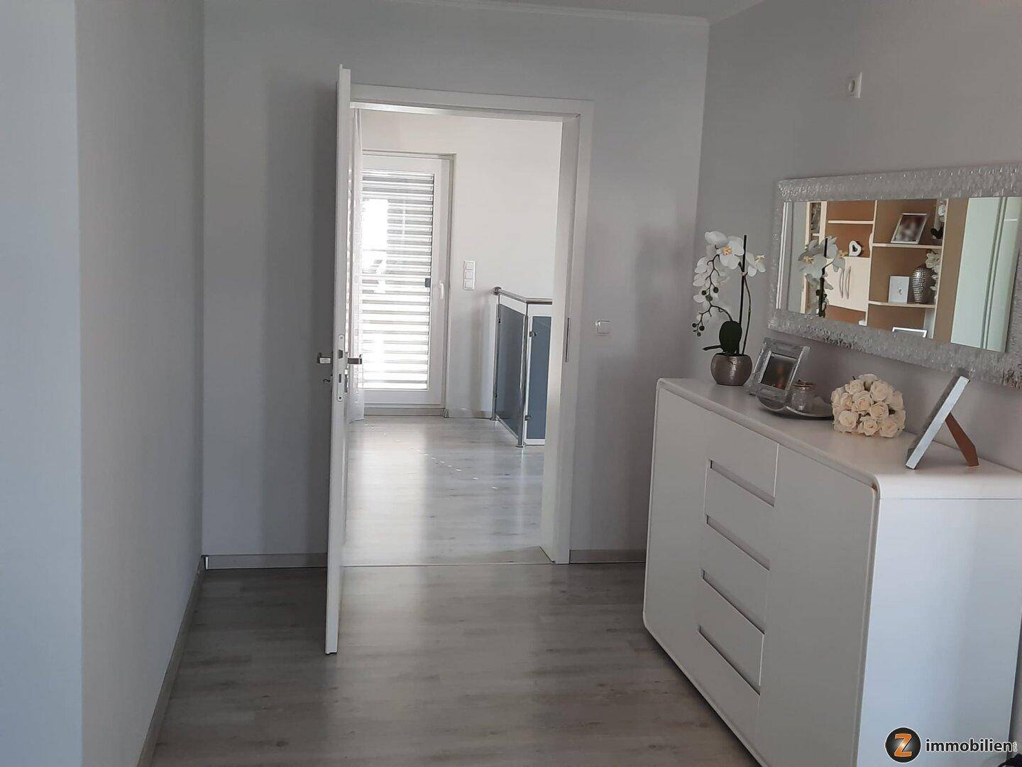 Heller Flur mit modernem Sideboard, Spiegel und Zugang zu weiteren Räumen.