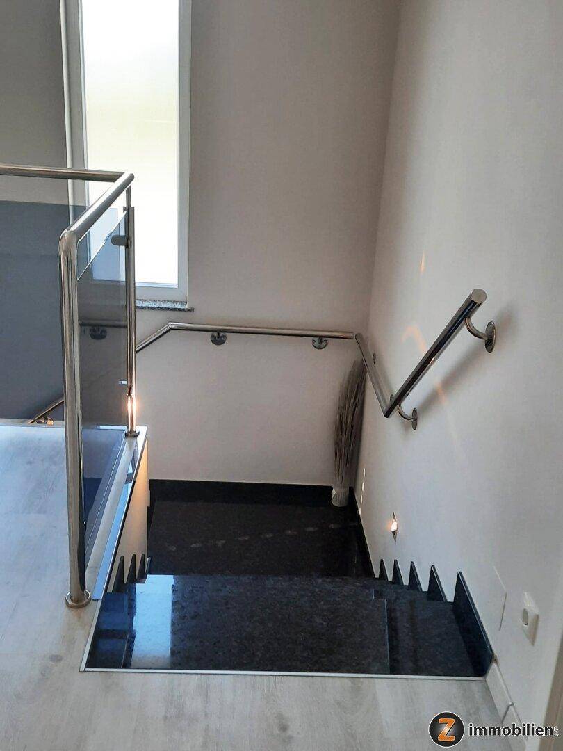 Blick von oben auf die moderne Treppe mit Glasgeländer und dunklen Stufen.