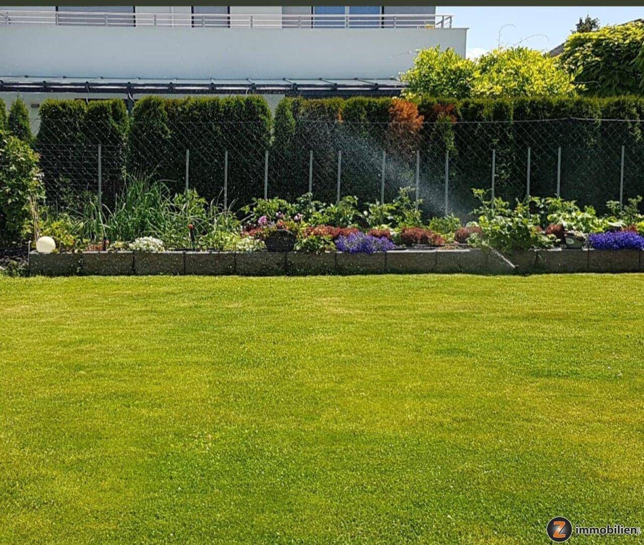 Gepflegter Garten mit Rasenfläche und einem bunten Blumenbeet entlang der Hecke.