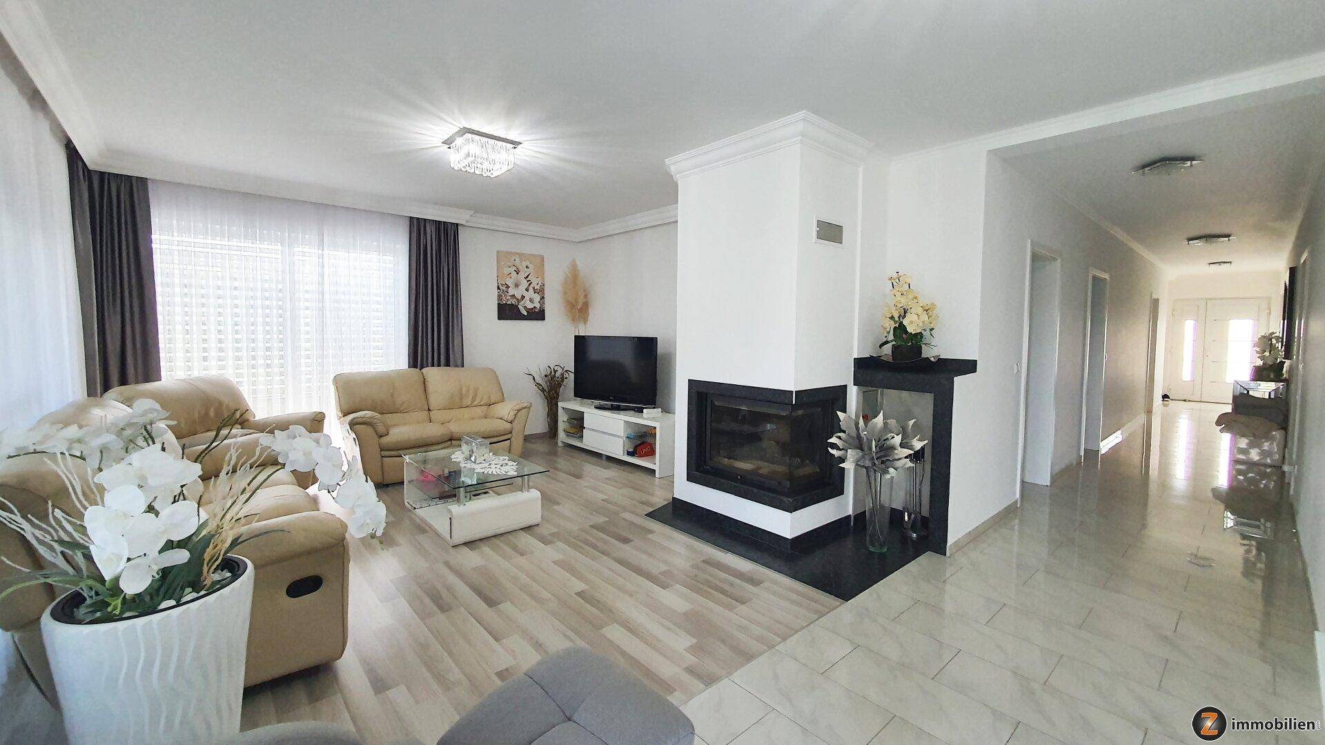 Geräumiges Wohnzimmer mit modernem Kamin, bequemen Sofas und hellem Boden.