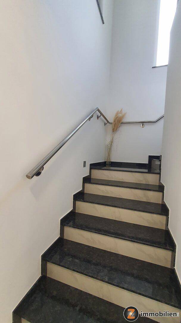 Moderne Treppe mit dunklen Granitstufen und Edelstahlgeländer, gut beleuchtet.
