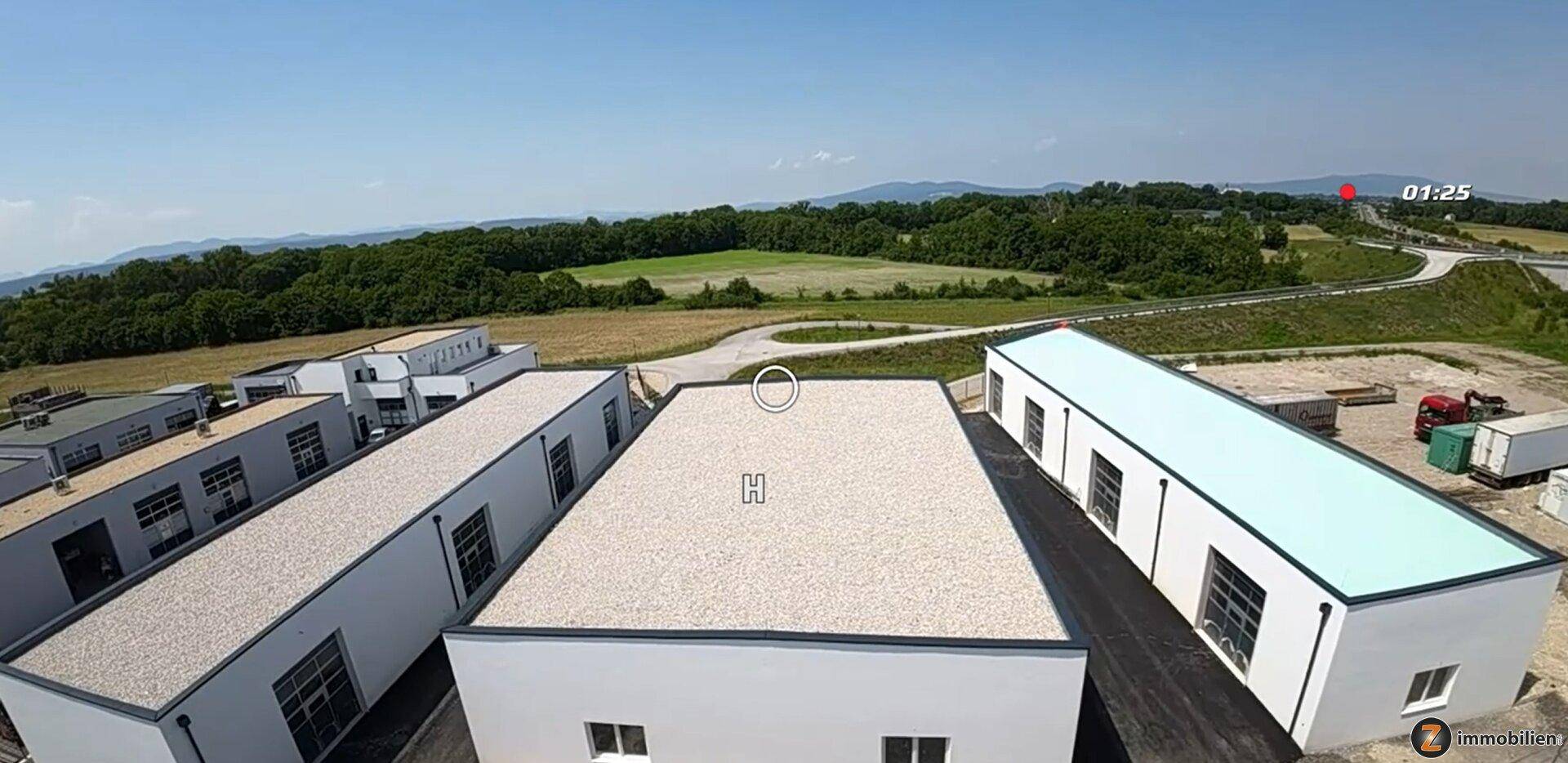 Luftaufnahme mehrerer neuer Gewerbegebäude mit Flachdächern, umgeben von grüner Landschaft und Hügeln.