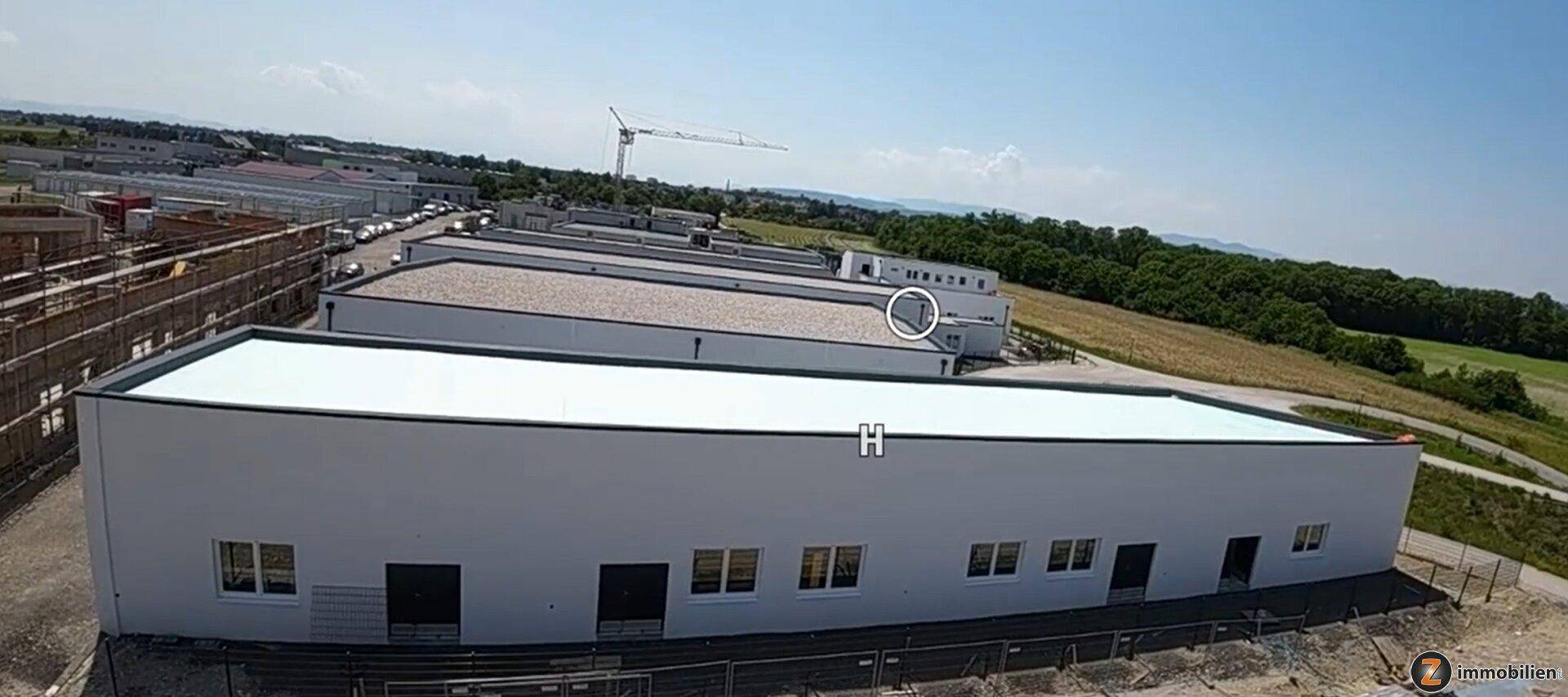 Luftaufnahme der Gewerbegebäude und des umliegenden Baugeländes mit weitem Blick in die Landschaft.