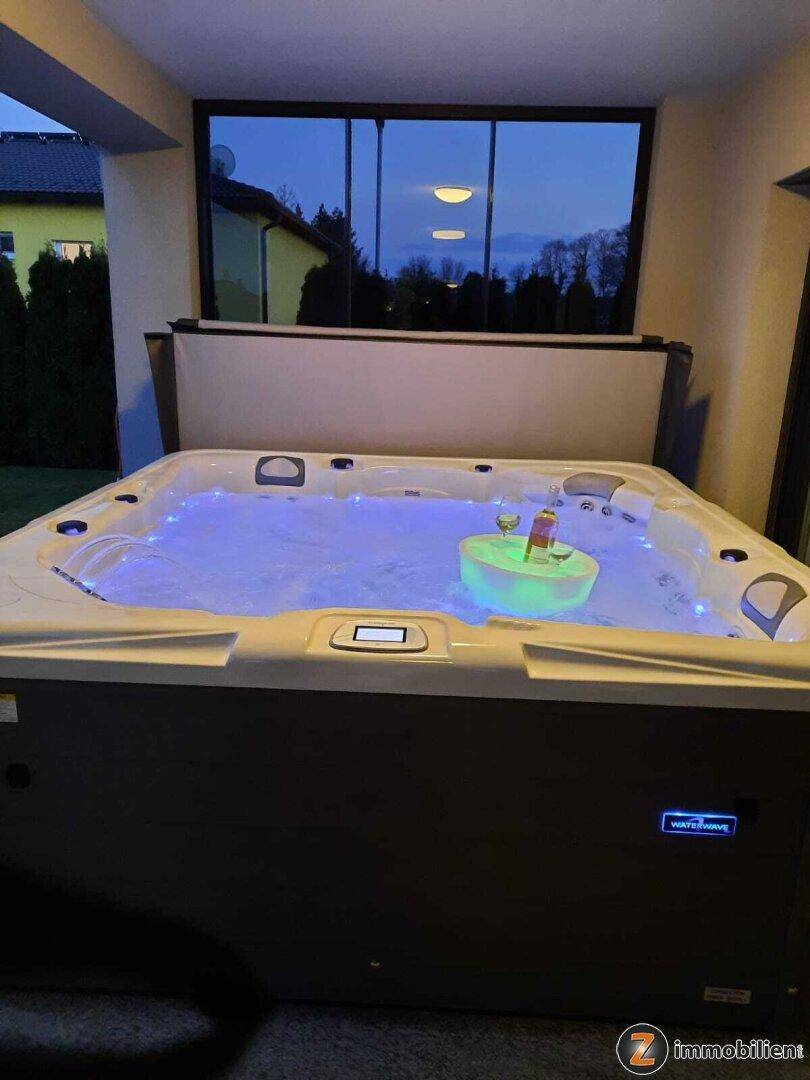 Beleuchteter Whirlpool auf der überdachten Terrasse mit Blick in die Ferne am Abend.