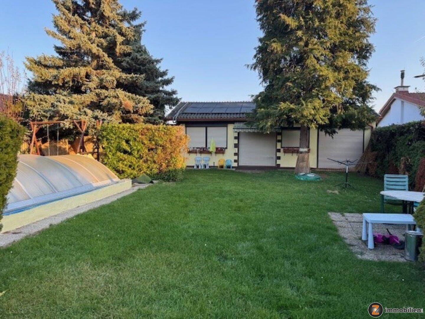 Gepflegter Garten mit großer Rasenfläche, hohen Bäumen und abgedecktem Poolbereich.