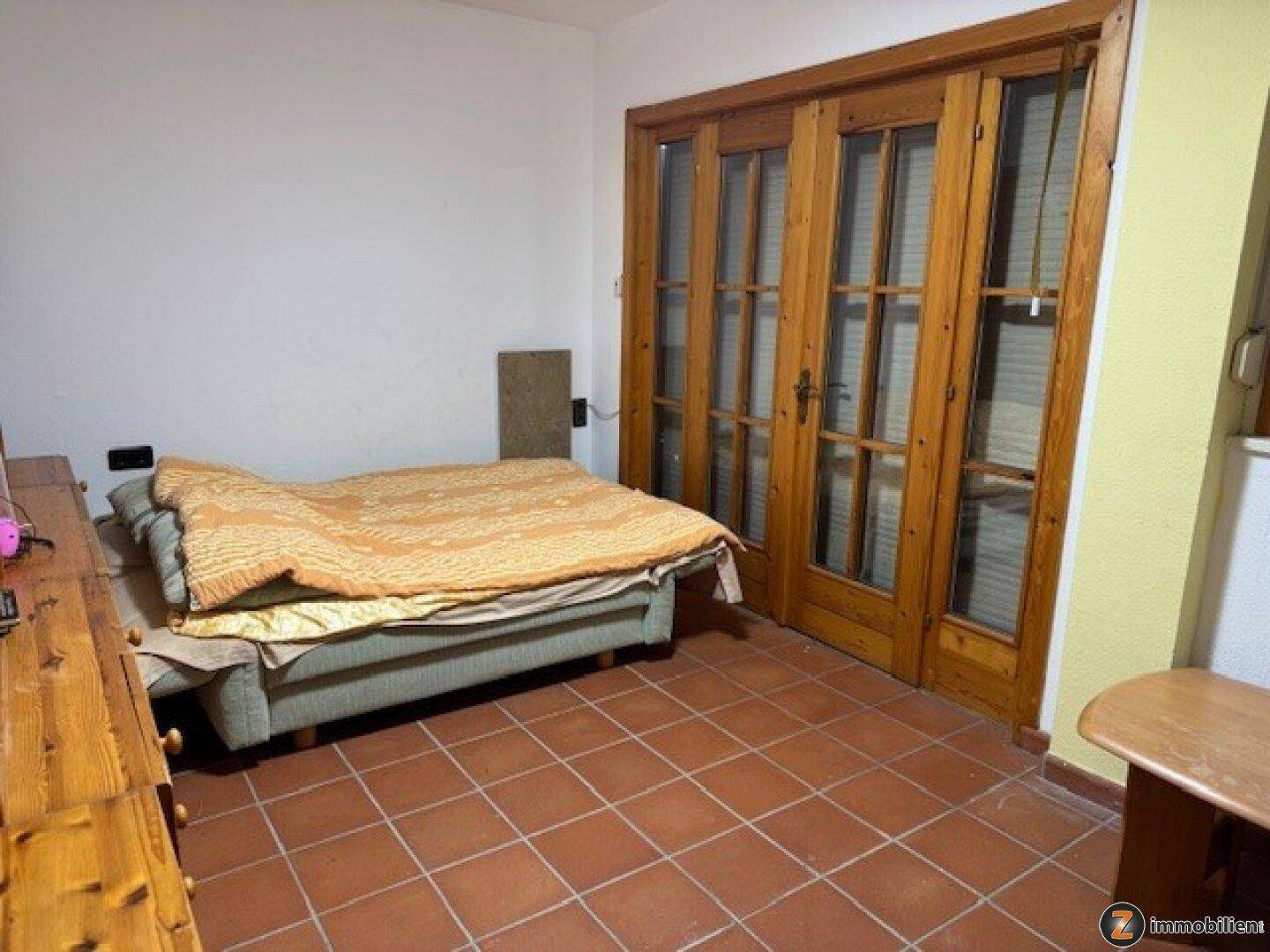 Schlafzimmer mit Terrakottafliesen, Holztüren und einfacher Einrichtung.