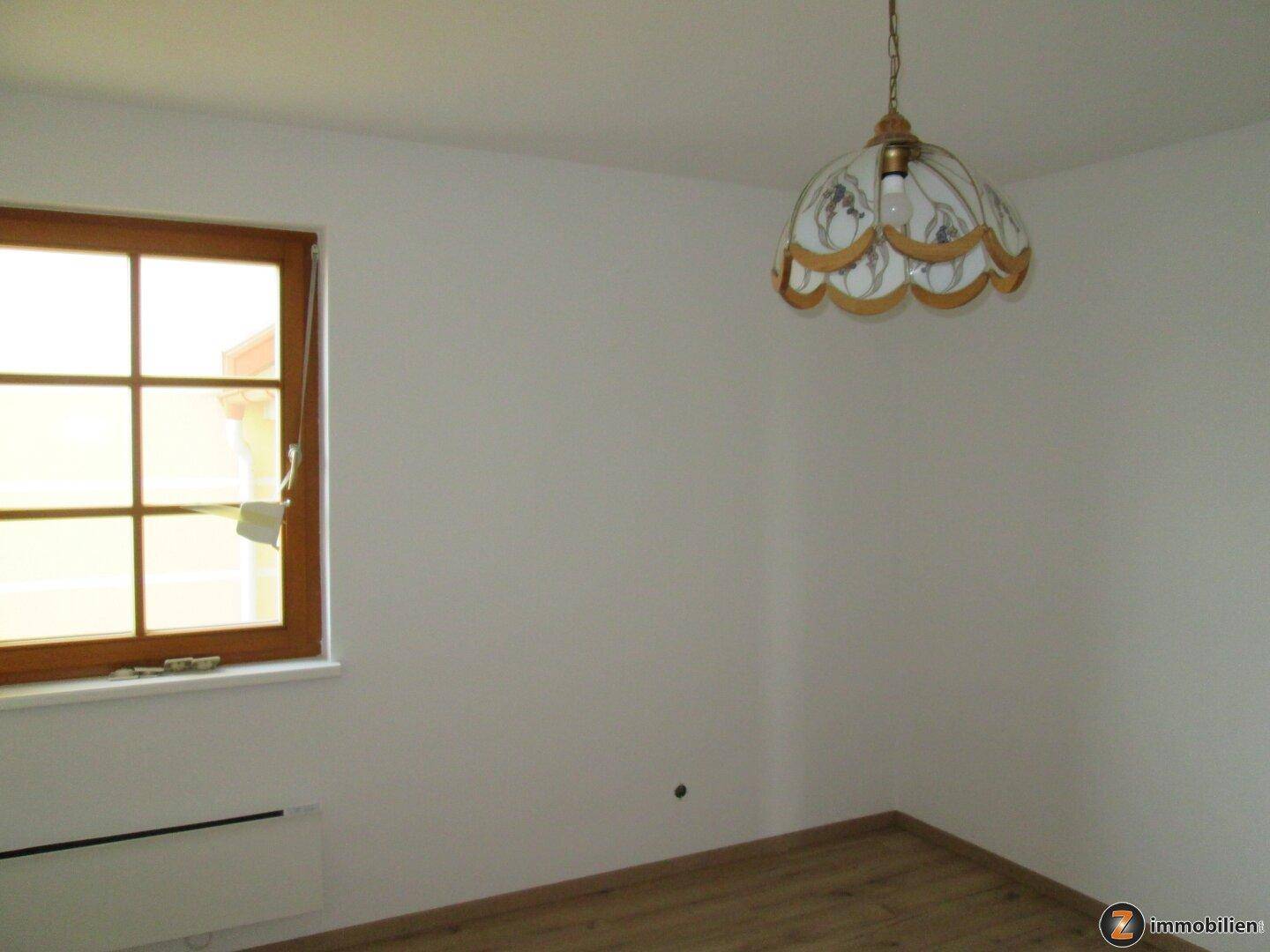 Schlafzimmer mit Laminatboden, Fenster und einer klassischen Deckenleuchte für gemütliches Ambiente.