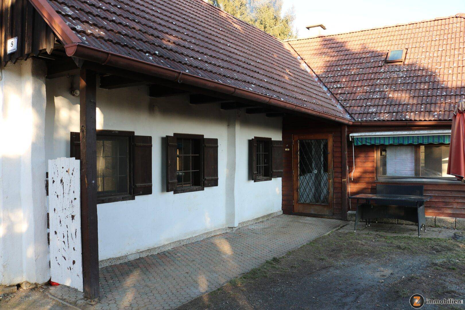 Seitenansicht des Landhauses mit gepflastertem Bereich und traditionellen Fensterläden.