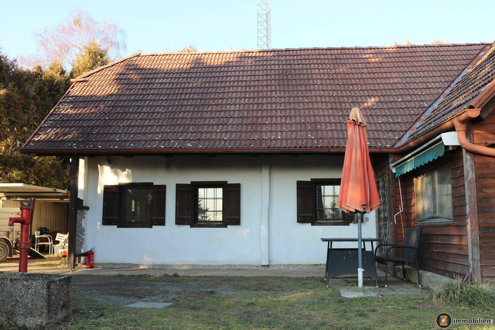 Kleiner gepflasterter Terrassenbereich neben dem Haus mit Sonnenschirm und Sitzgelegenheiten.