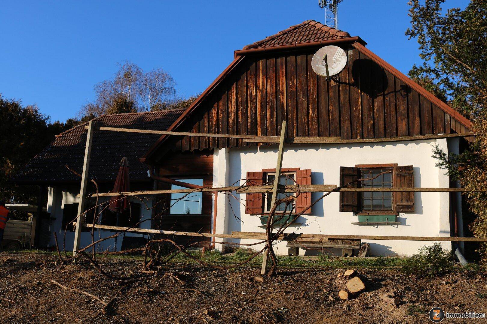 Traditionelles Landhaus mit Holzgiebel und weißer Fassade, umgeben von ländlicher Landschaft.