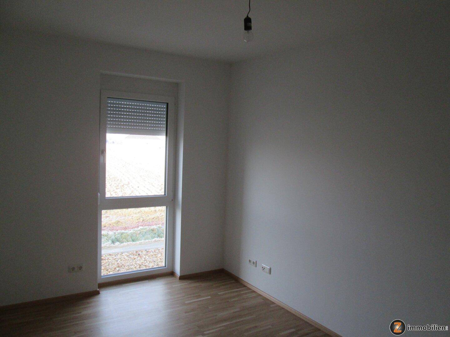 Helles Schlafzimmer mit Holzboden, weiß gestrichenen Wänden und großem Fenster.