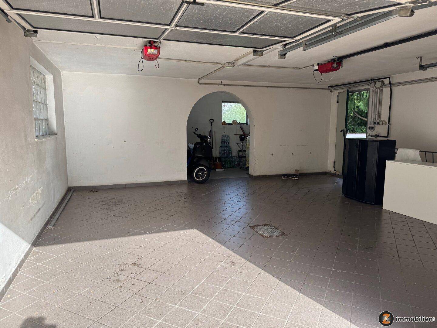 Geräumige Garage mit Fliesenboden und Zugang zu einem weiteren Abstellraum.