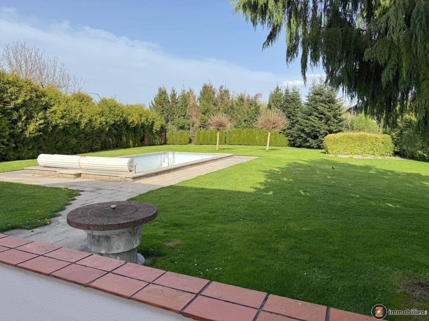 Großer Garten mit Rasenfläche, umgeben von Hecken und einem Außenpool.