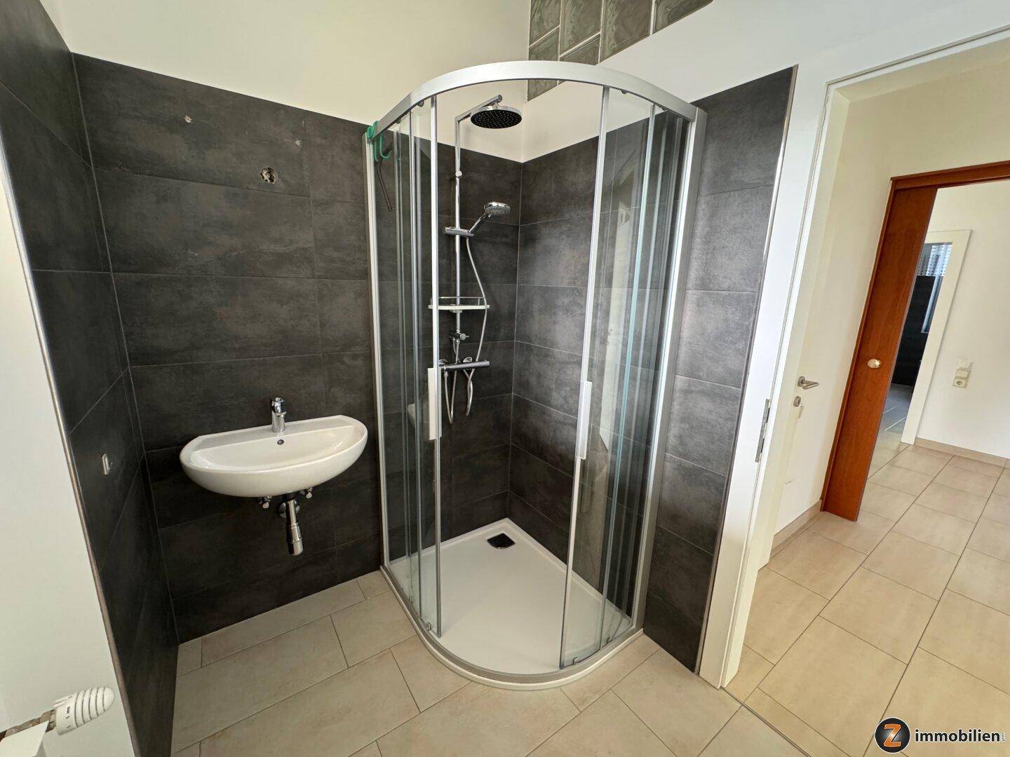 Kleines Badezimmer mit Duschkabine und Waschbecken, modern gefliest.