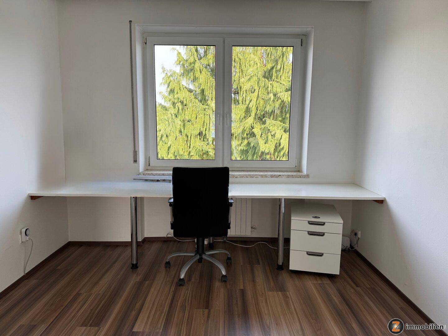 Helles Arbeitszimmer mit großem Fenster und Schreibtisch mit Blick ins Grüne.