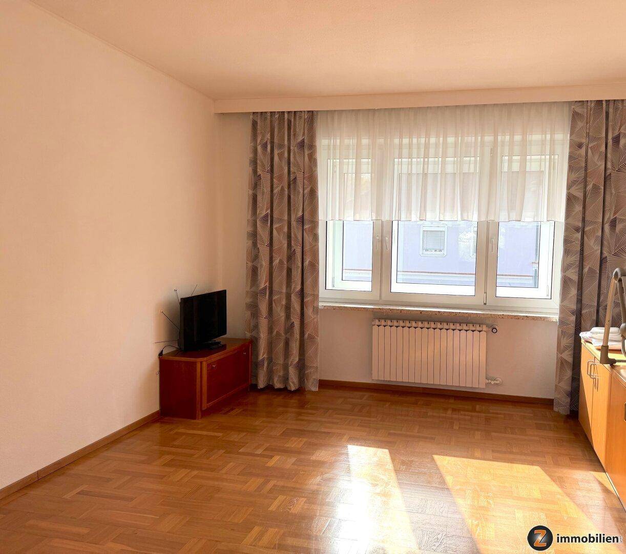 Wohnzimmer mit Parkettboden, Fenster und Vorhängen, bereit zur Einrichtung.