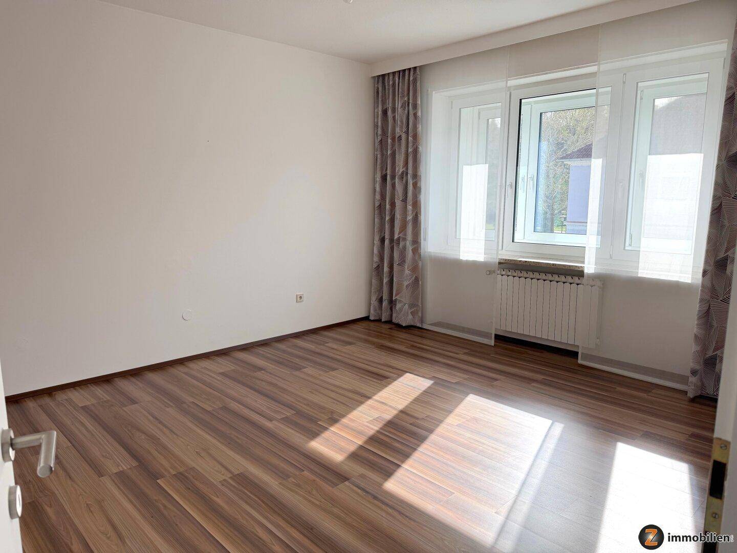 Schlafzimmer mit Laminatboden und großem Fenster, das viel Licht hereinlässt.