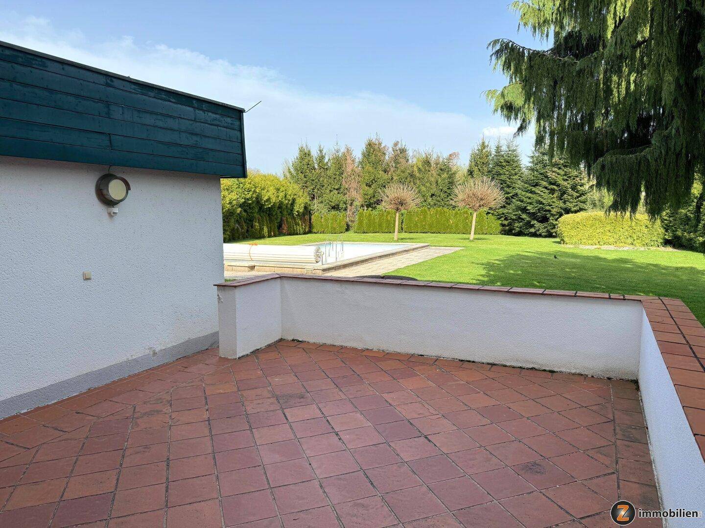 Große geflieste Terrasse mit Blick auf den Garten und den Swimmingpool.