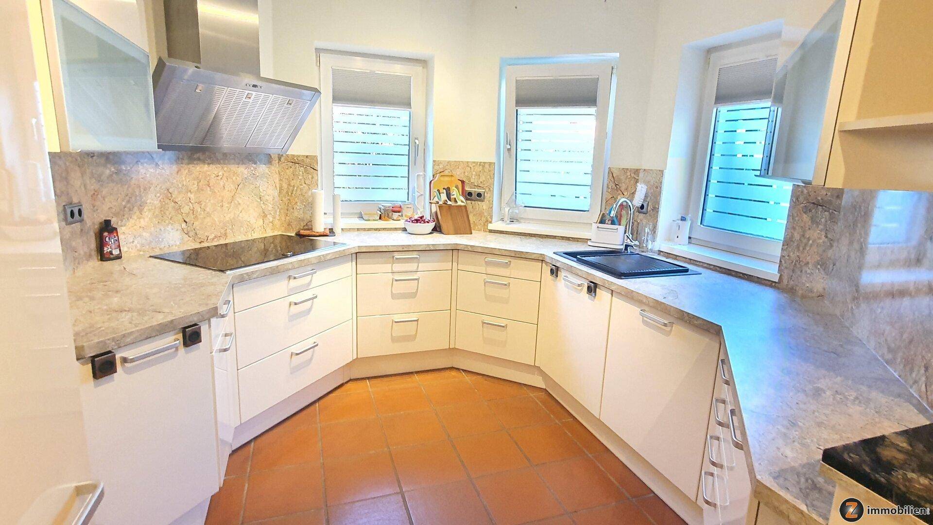 Moderne Küche mit weißen Schränken, Granitarbeitsplatten, Induktionskochfeld und Terrakottafliesen am Boden.
