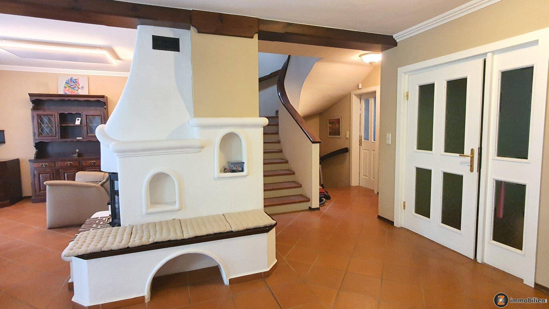 Geräumiger Flur mit einem imposanten Kaminofen, einer geschwungenen Treppe und Terrakottafliesen am Boden.