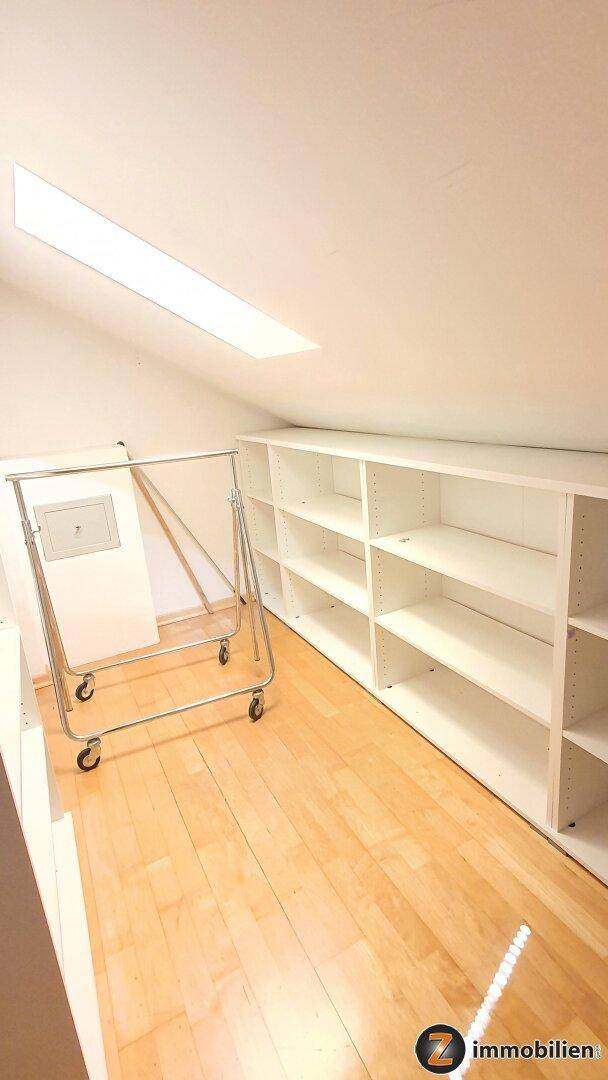 Heller Dachbodenraum mit Dachschräge, Oberlicht, Holzfußboden und praktischen weißen Regalsystemen.