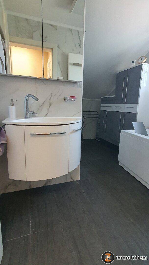Modernes Badezimmer mit elegantem Einzelwaschbecken, großem Spiegel und dunklem Fliesenboden.
