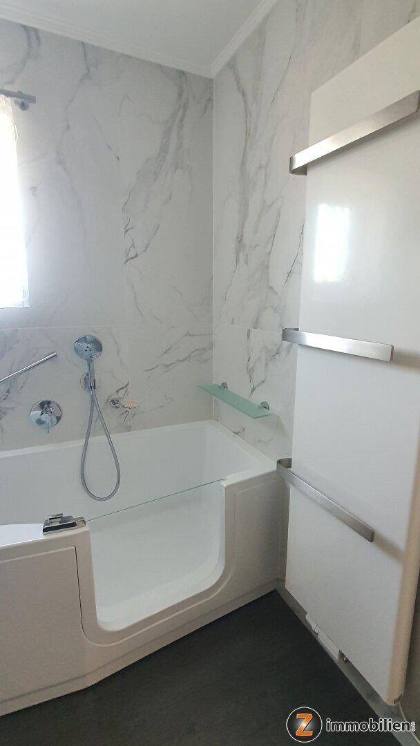 Helles Badezimmer mit barrierefreier Badewanne, Marmorfliesen und einem beheizten Handtuchhalter.