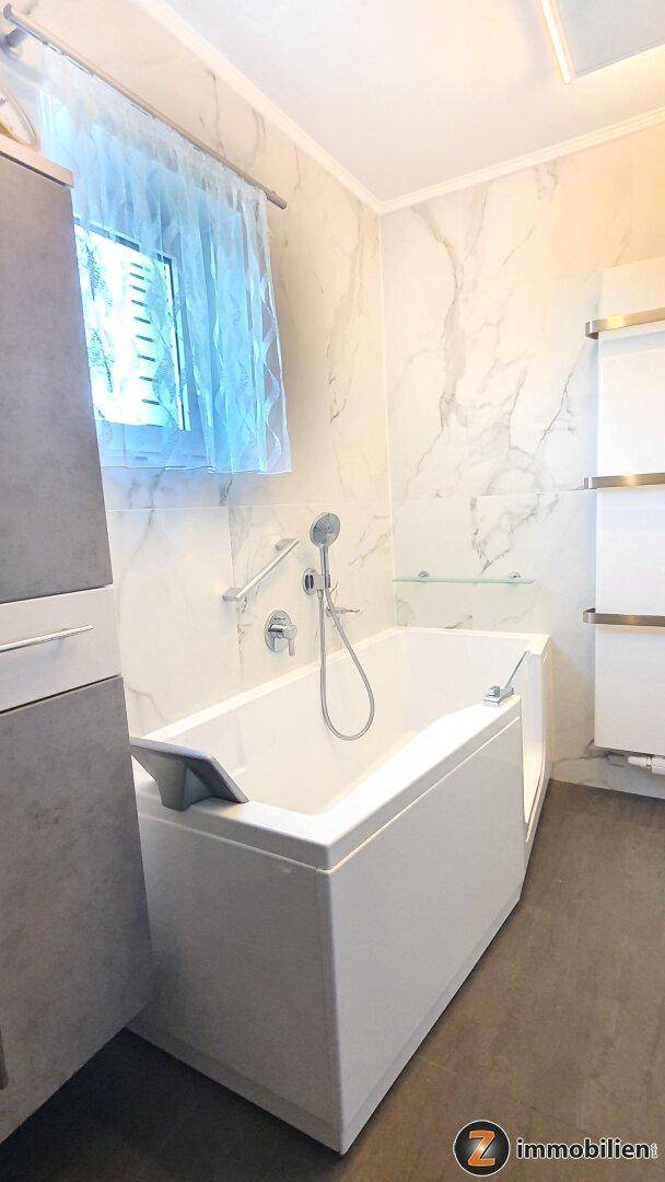 Modernes Badezimmer mit Badewanne, Marmorfliesen, Fenster und beheiztem Handtuchhalter für Komfort.