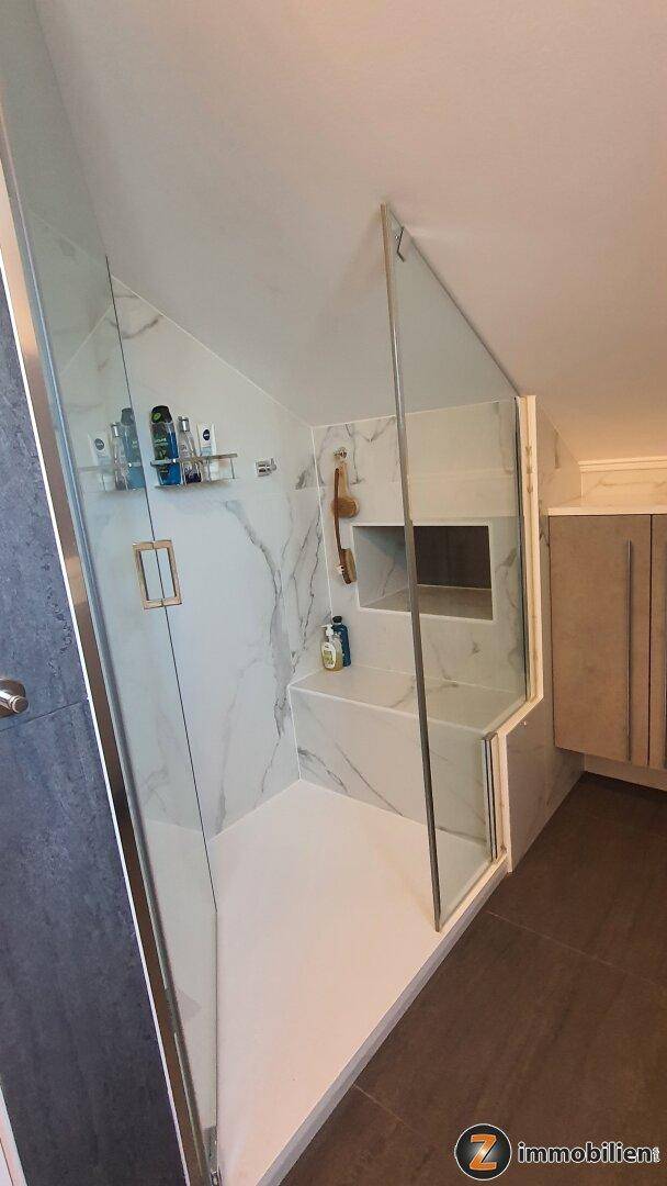 Elegantes Badezimmer mit begehbarer Dusche, Glasabtrennung, Marmorfliesen und dunklem Fliesenboden.