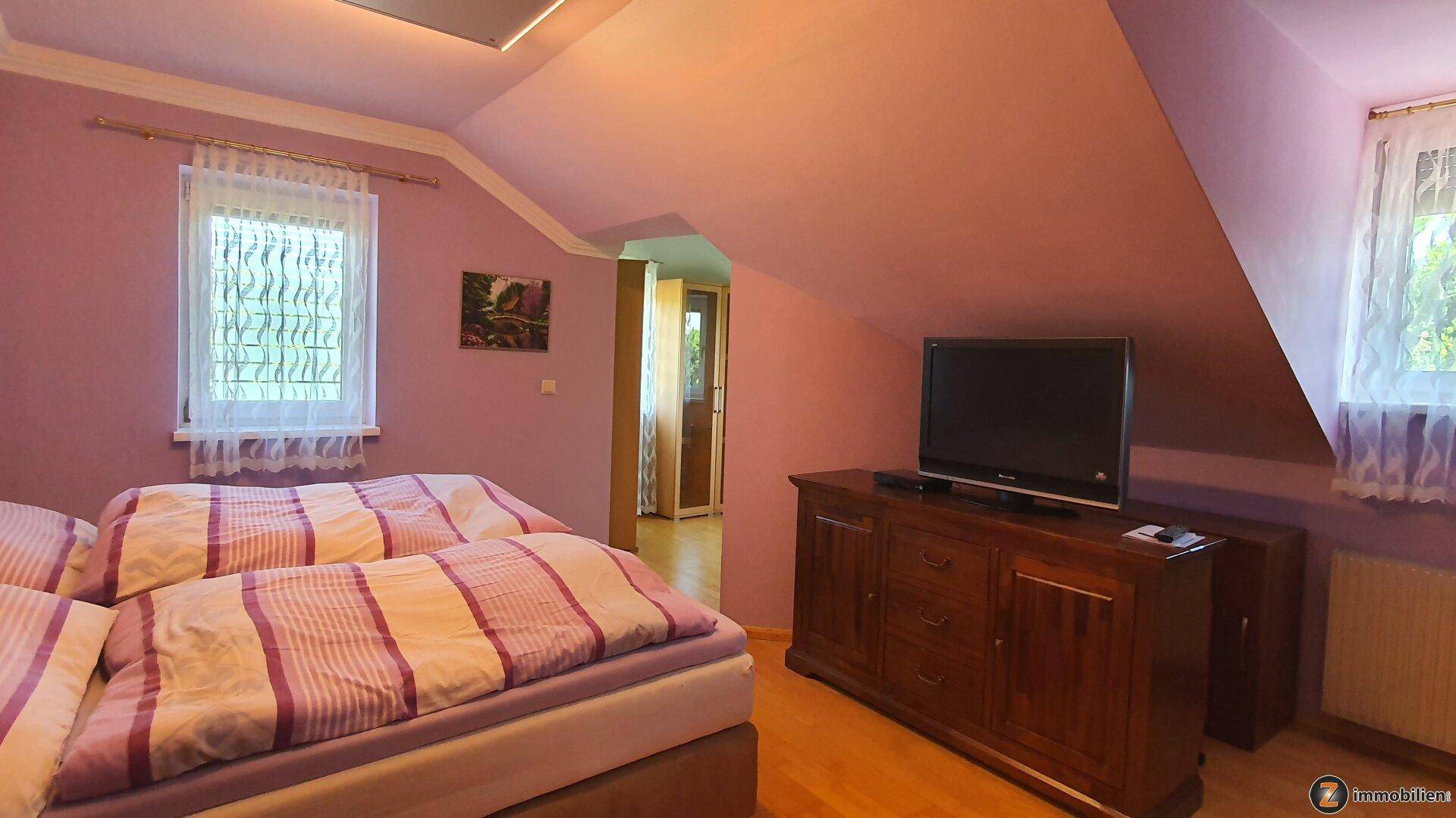 Gemütliches Schlafzimmer mit zwei Einzelbetten, Fernseher auf einer Kommode und Dachschräge.