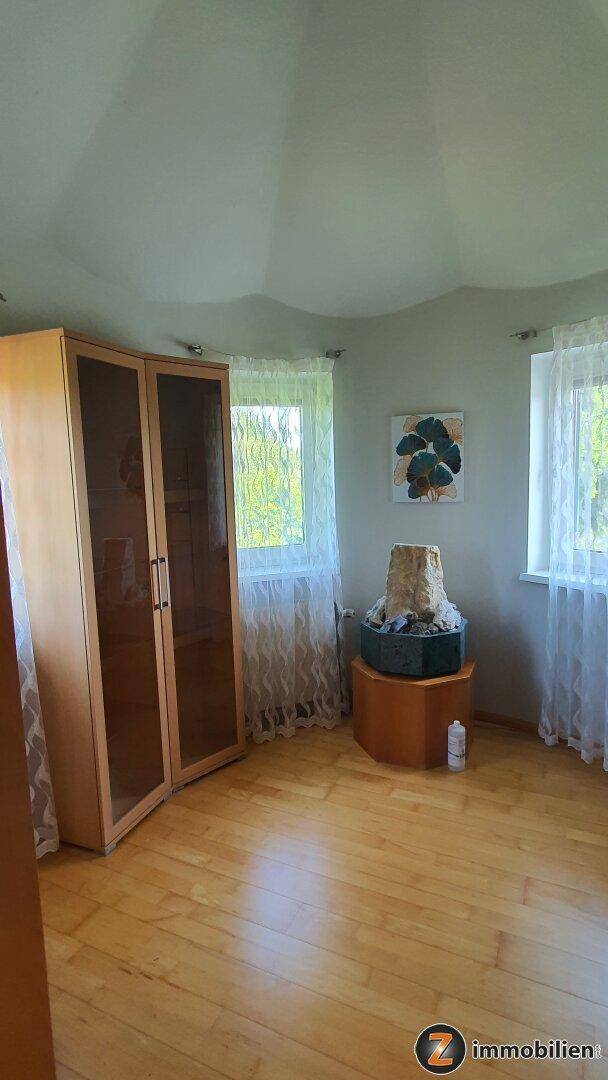Helles Zimmer mit Holzboden, zwei Fenstern und einer einzigartigen wellenförmigen Decke.