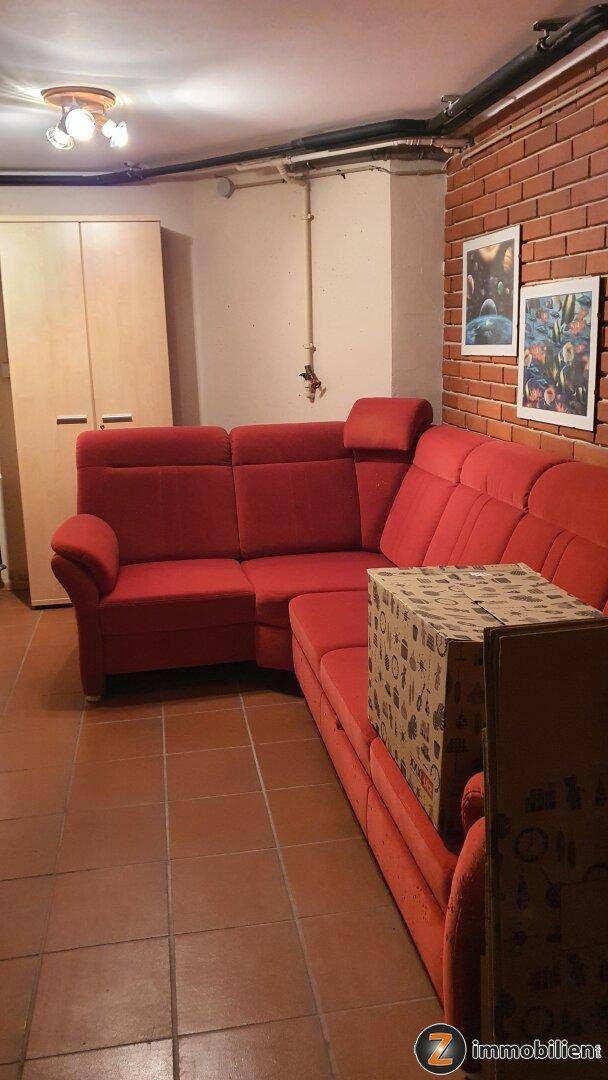 Kellerraum mit großer roter Eckcouch, Ziegelwand und Fliesenboden, ideal als Hobbyraum.