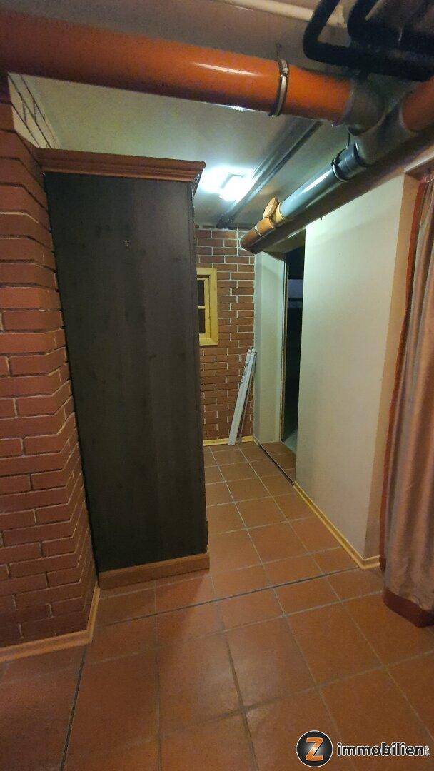 Kellerbereich mit Ziegelwänden, Fliesenboden und sichtbaren Rohren, genutzt als Abstellfläche.
