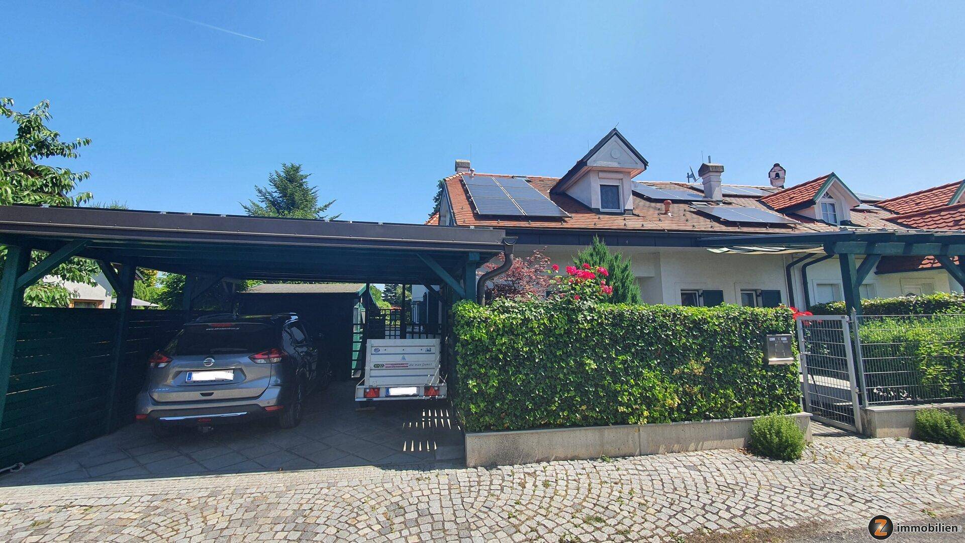 Haus mit Carport, Solaranlage auf dem Dach und gepflegter Hecke im Vorgartenbereich.