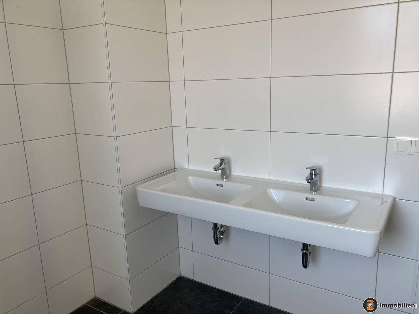 Modernes Badezimmer mit Doppelwaschbecken und großen weißen Wandfliesen.