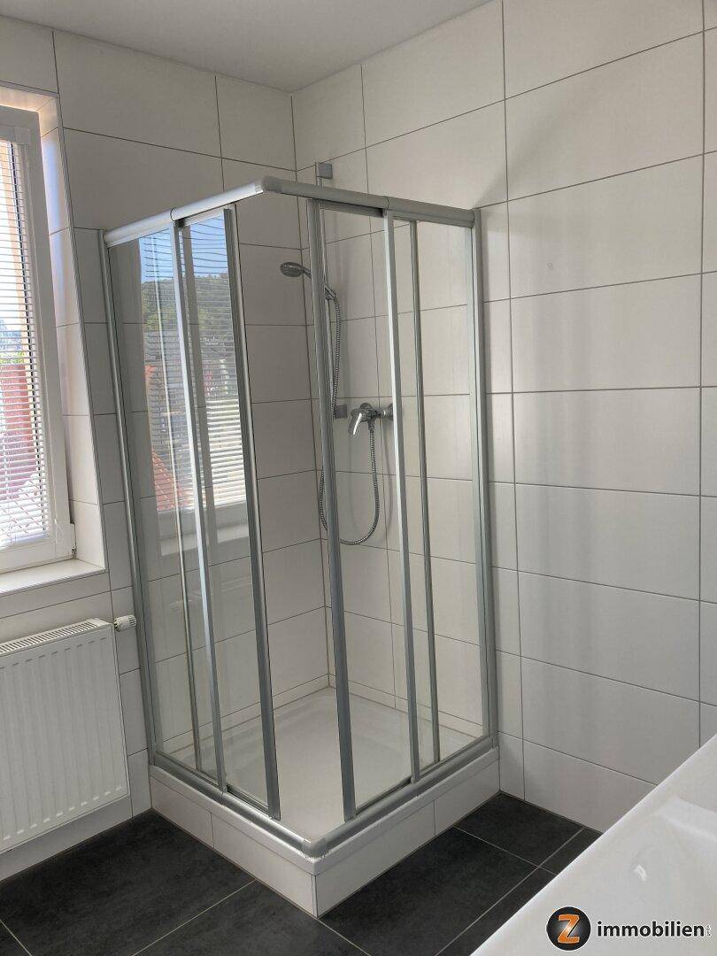 Helles Badezimmer mit Duschkabine, Fenster und weißen Wandfliesen.