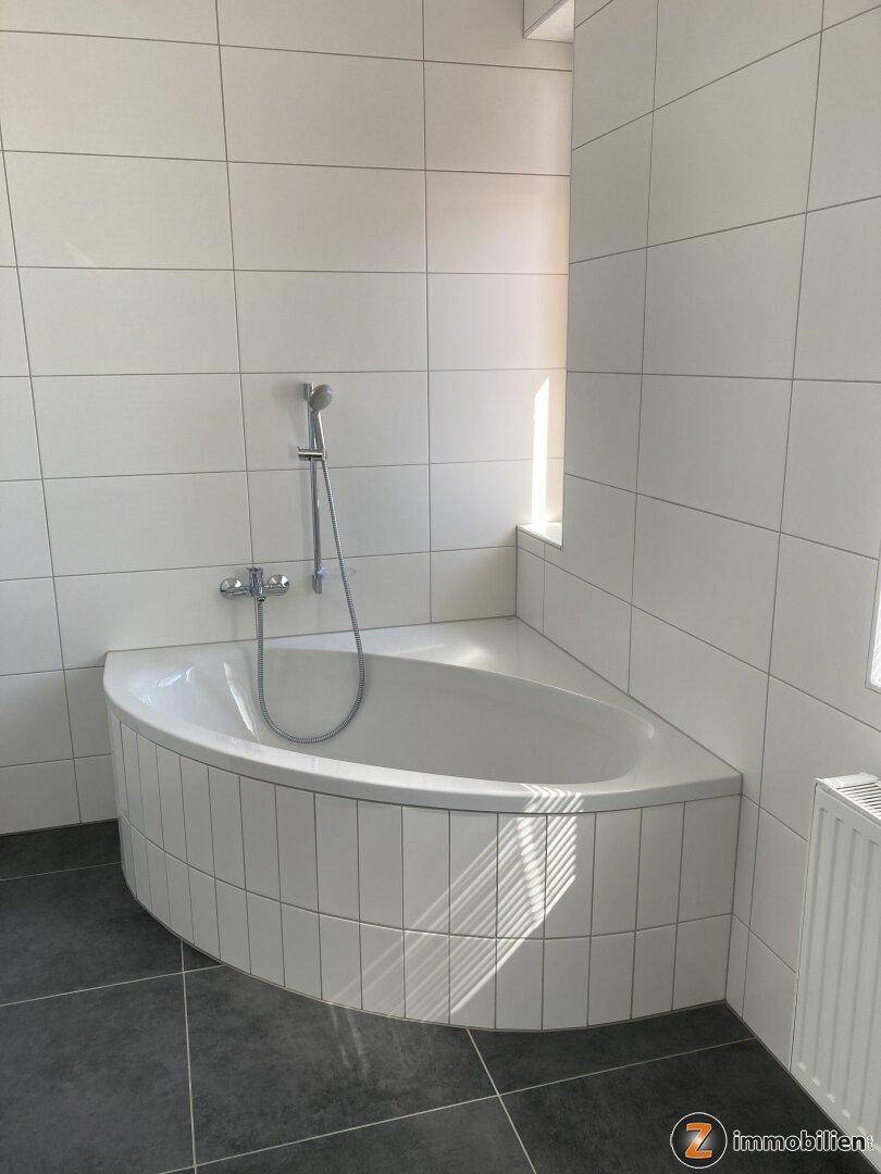 Geräumiges Badezimmer mit Eckbadewanne und weißen Fliesen, gut beleuchtet.