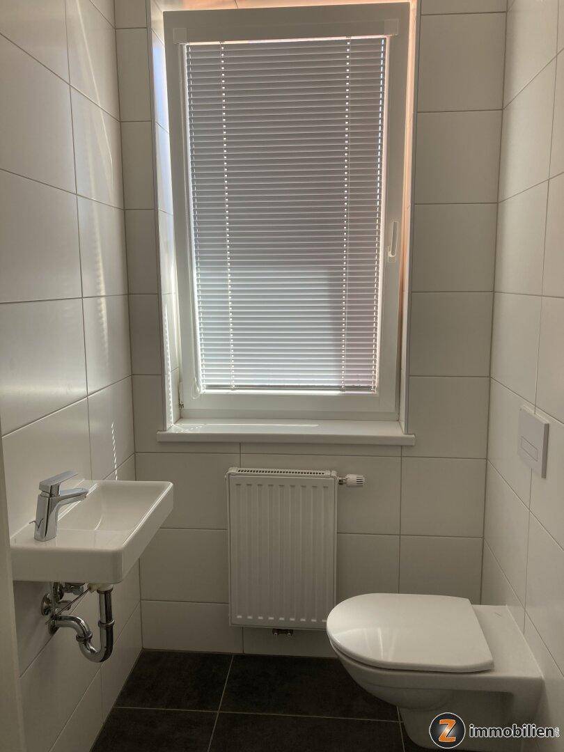 Separates Gäste-WC mit Fenster, wandhängendem WC und kleinem Waschbecken.